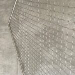 Stainless steel rope mesh panel with a diamond aperture, installed against a concrete wall