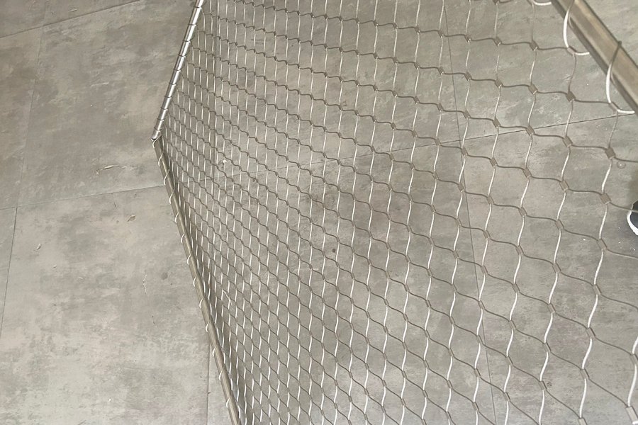 Stainless steel rope mesh panel with a diamond aperture, installed against a concrete wall
