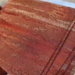 Fine woven metal fabric in copper tones, held up to the light, showing the crimped weave